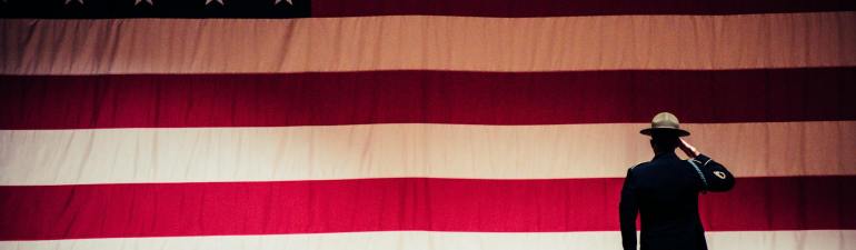 man standing on stage facing an american flag